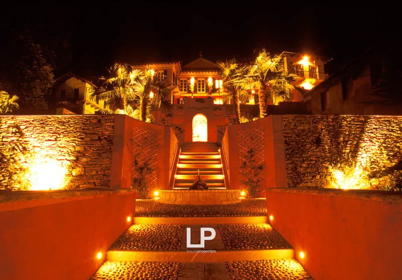 Stairway leading to entrance of building, arched entrance, large stone walls, illuminated by yellow lights, lush palm trees