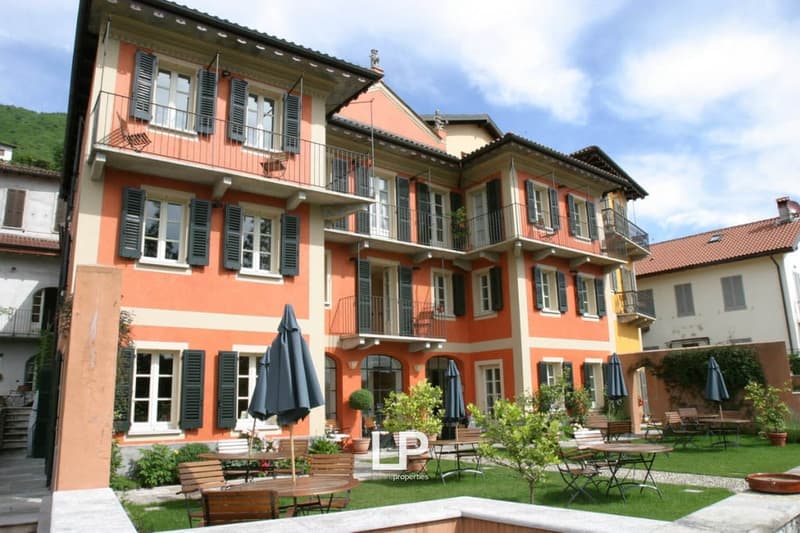 Three story hotel, orange and white exterior, balconies, garden with tables and chairs