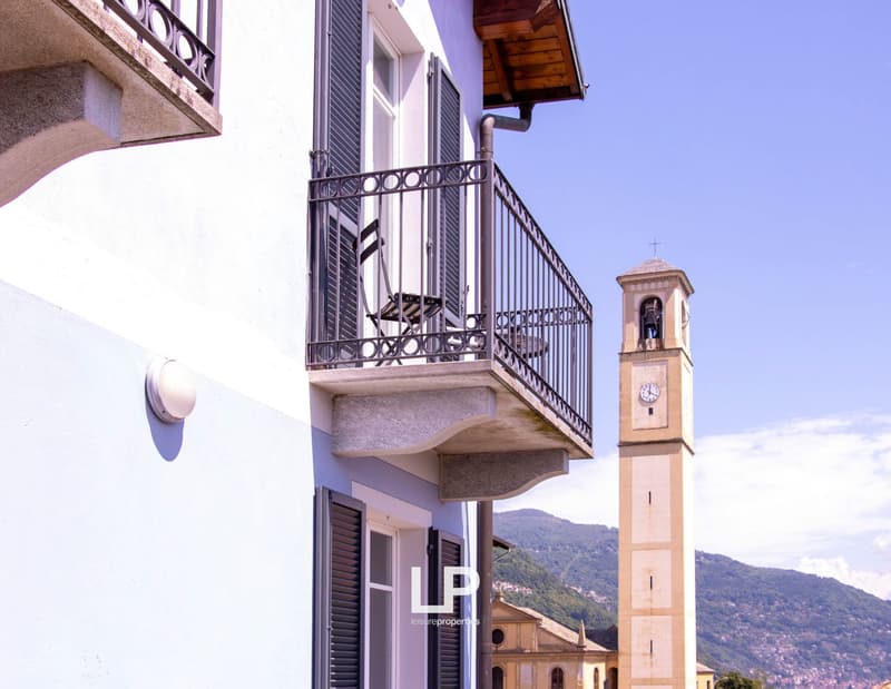 Balcony with metal railing, table and chair, bell tower in background, white building