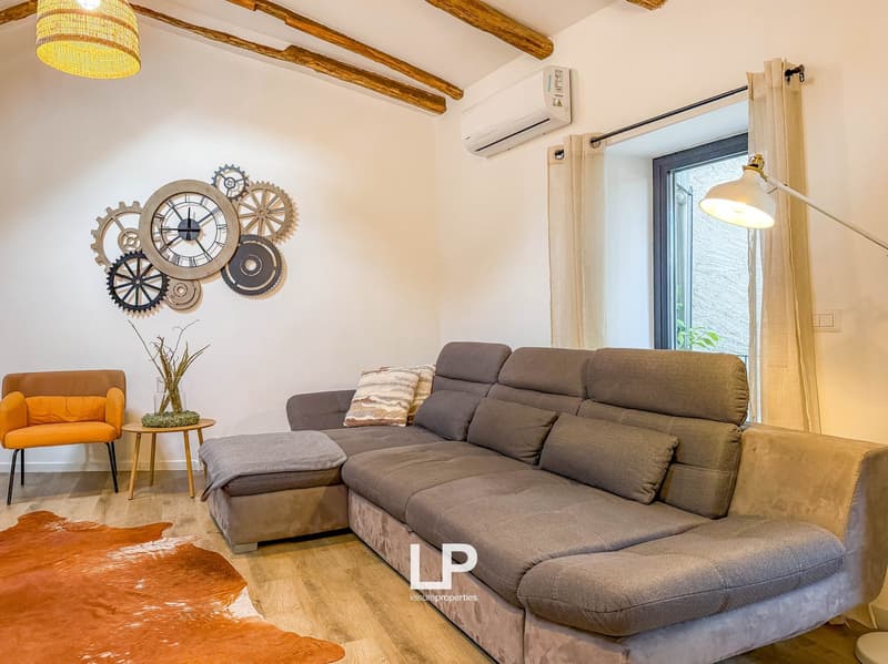 L-shaped sofa, wooden table, orange chair, carpet, decorative gear art on wall, window with light, air conditioner on wall