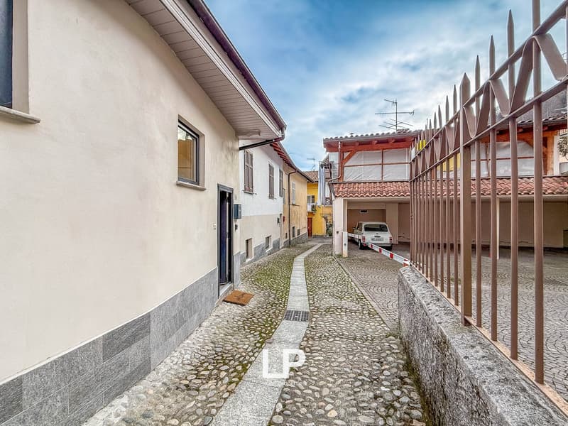 Narrow cobblestone alley, white buildings, a parked car in a garage, metal gate