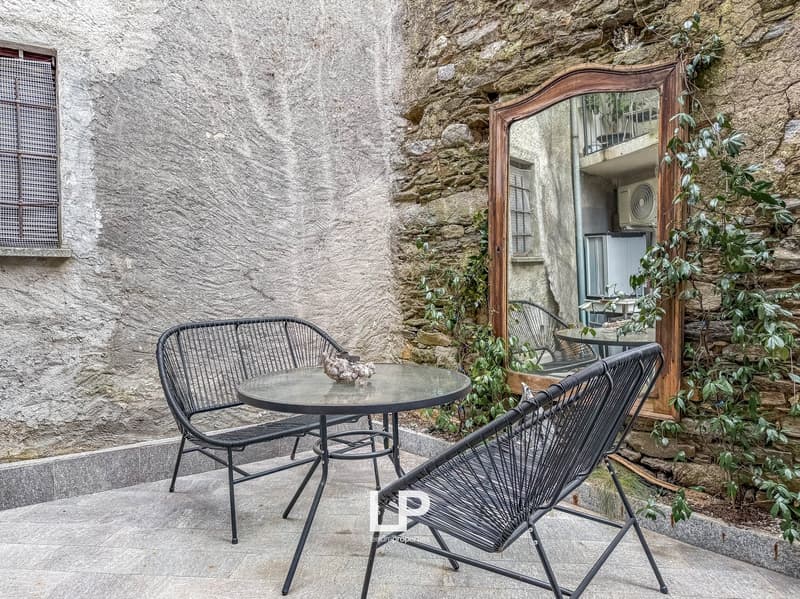 A small outdoor area with a stone wall, a glass table, 2 chairs, and a mirror attached to the wall.