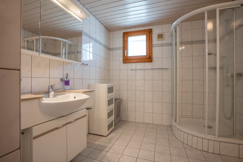 Bathroom with a sink, shower enclosure, tiled walls and floor, cabinet with drawers, and a trash bin.