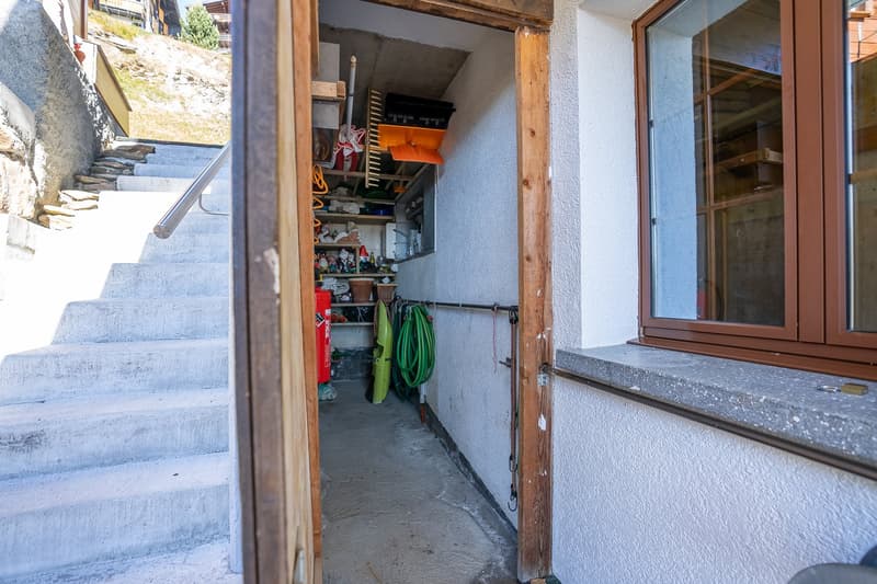Narrow corridor leading to storage room with shelves and various items, stairs and window