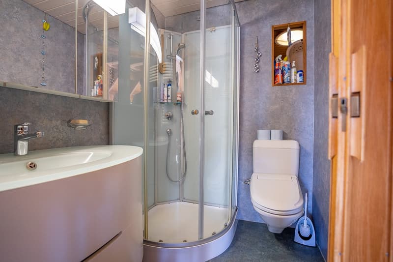modern bathroom with shower stall, sink with drawers, toilet, mirror, wooden door
