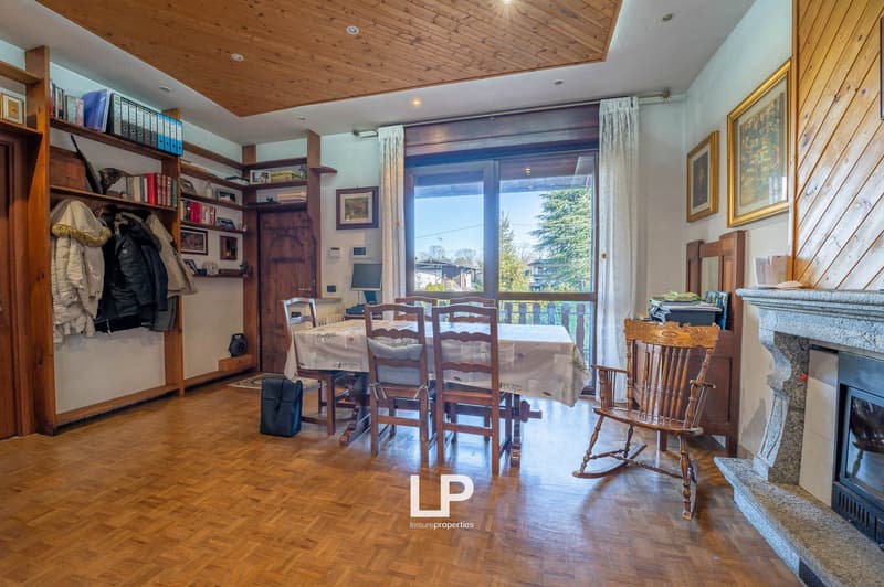 Dining room with table, chairs, fireplace, balcony, wooden flooring, bookshelves, coat rack, curtains, rocking chair