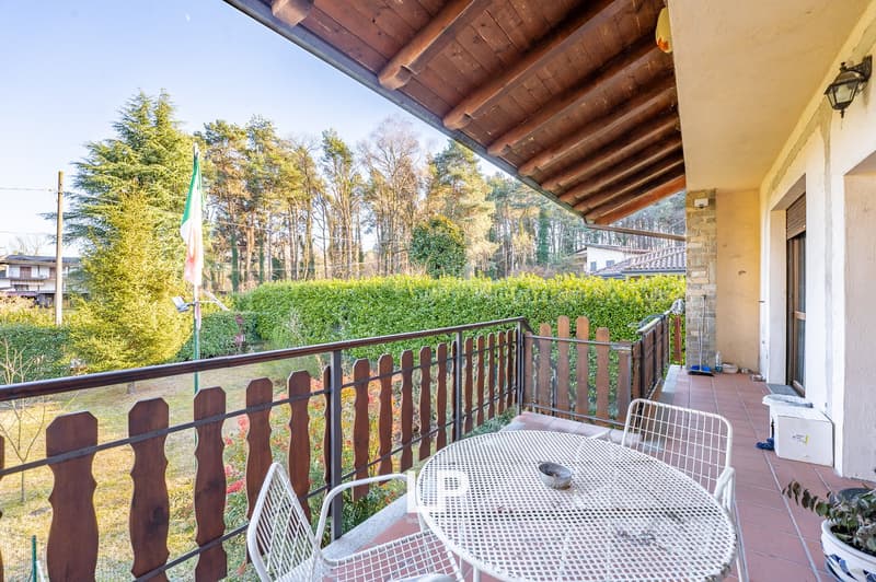 Wooden railings on balcony, metal table with 4 chairs, wooden floor, Italian flag, green vegetation view