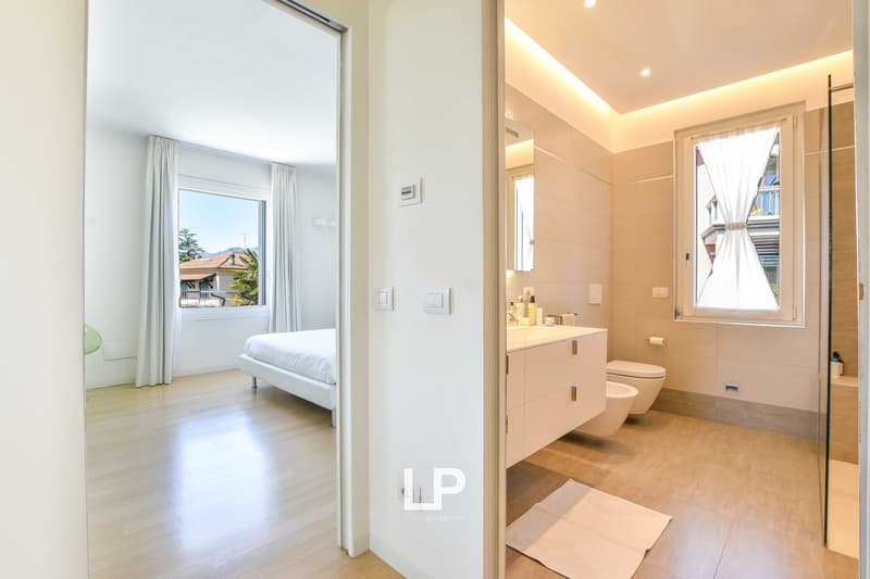 modern bathroom with large window, double sink, bathtub, toilet, and glass door shower