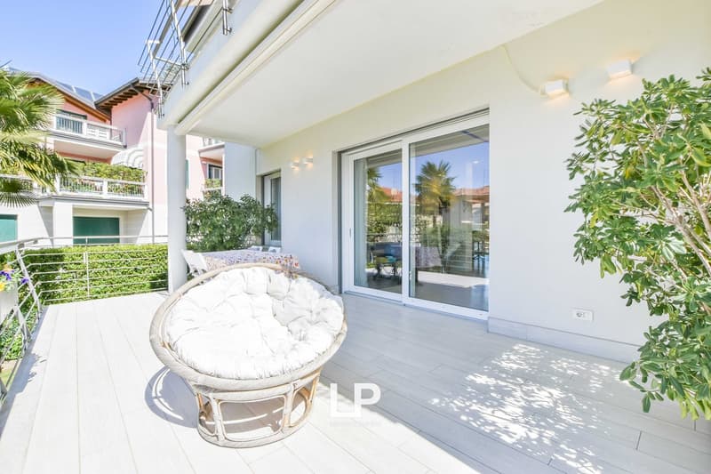 Spacious apartment with a balcony, large windows, and a cozy seating area with a wicker chair. The apartment has a modern, open layout with a view of the surrounding greenery.