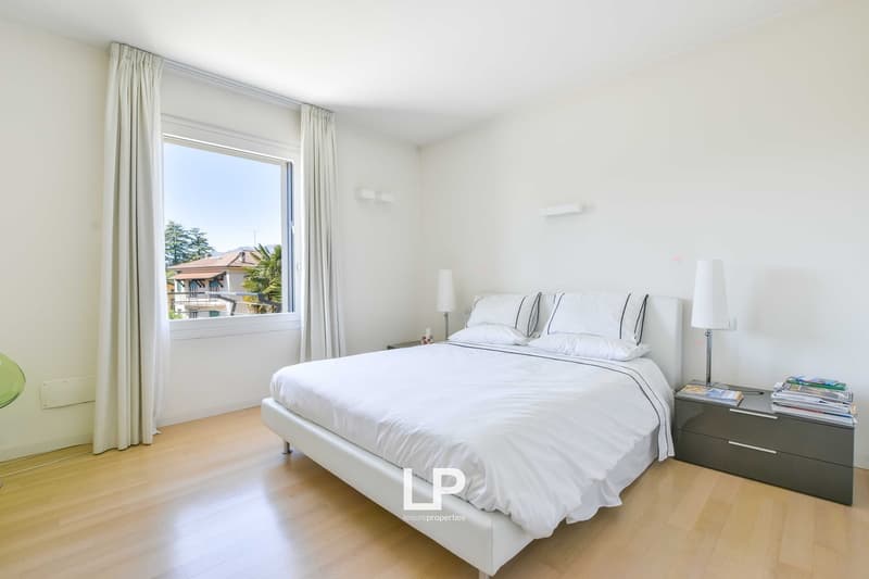 modern interior, white walls, wooden floor, bed, bedside tables with lamps, large window with curtains, night stand with books, power outlet