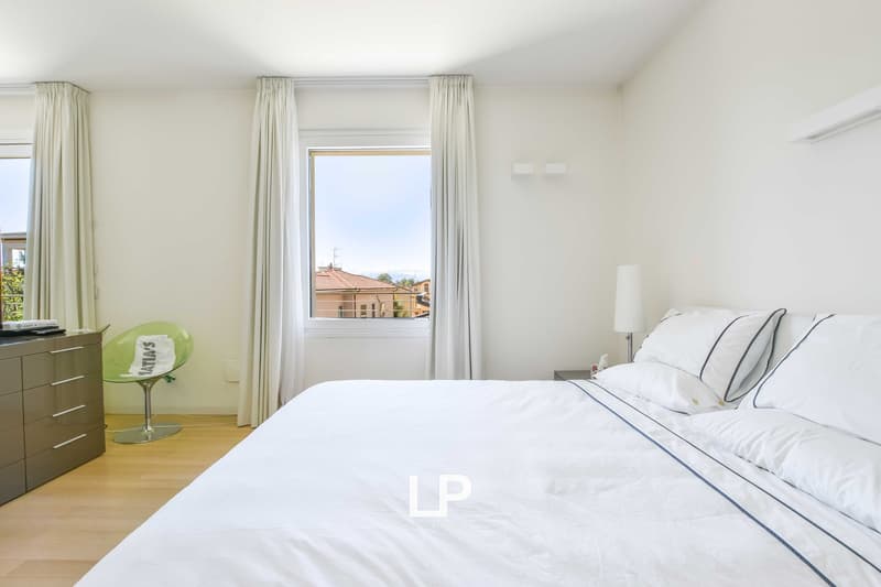 modern bedroom with white walls and bed, wooden floor, chair, night stand, lamp, windows with curtains