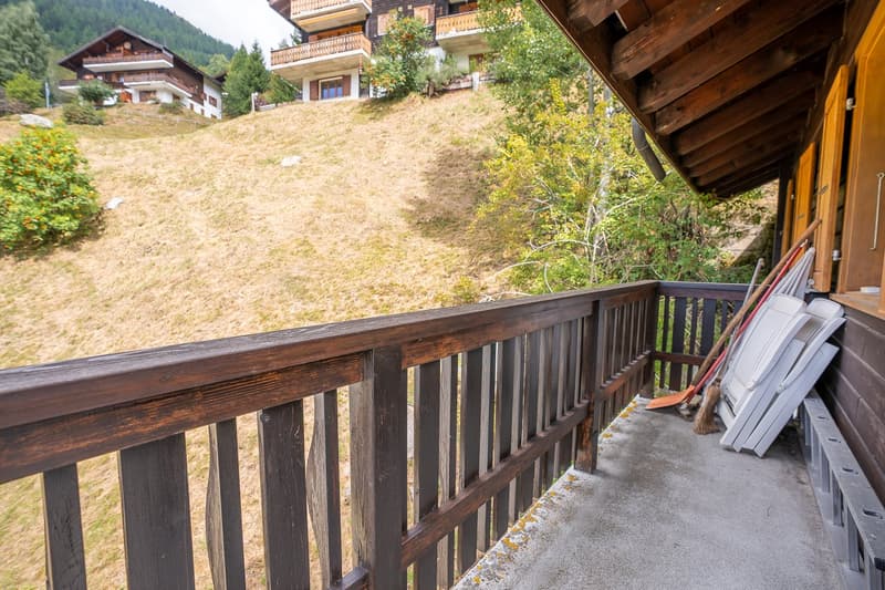 wooden balcony, view of a grassy slope with houses and trees