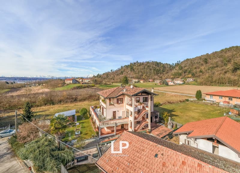 Villa with multiple levels, tiled roof, large windows, several balconies, surrounded by a garden, solar panels installed