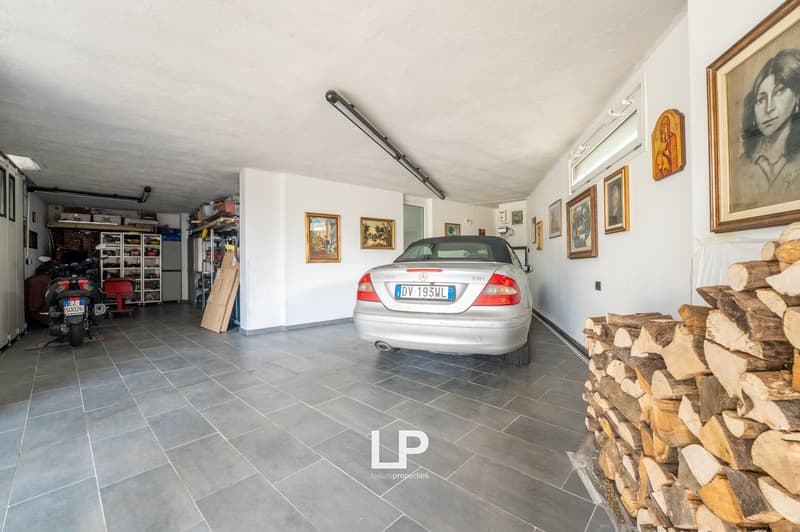 Tiled floor, vehicle parked inside, a pile of wood on one side, shelves on the side, a motorcycle against the wall.