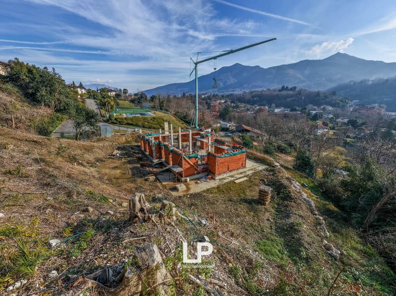 construction of a house with raised ground floor, brick walls, crane, mountain landscape