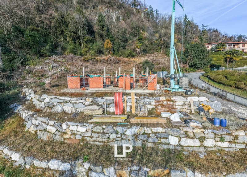 Building site in progress, foundation of a house with red brick wall, stones, steel beam, crane, road, trees