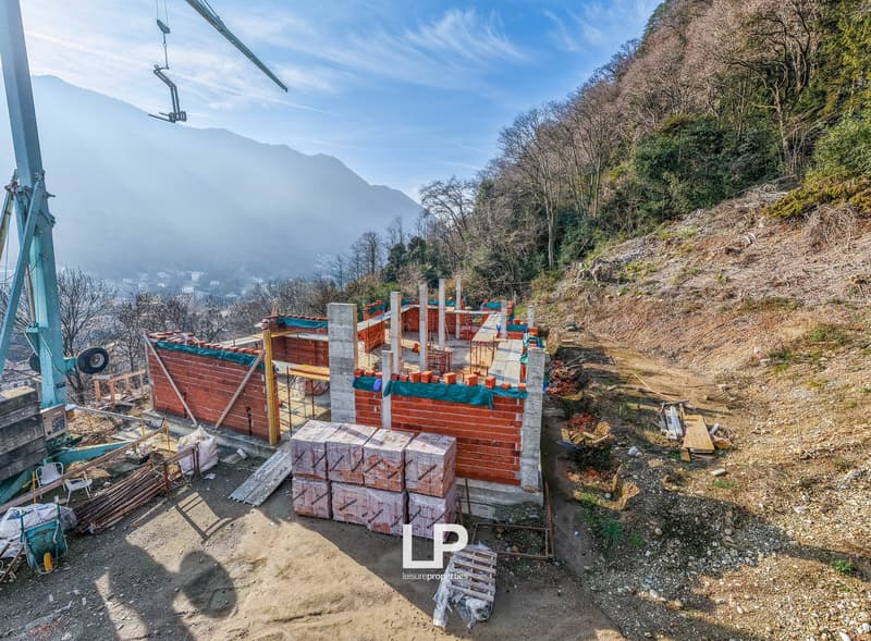 House under construction, with red brick walls, foundation in concrete, building materials nearby, crane in the distance