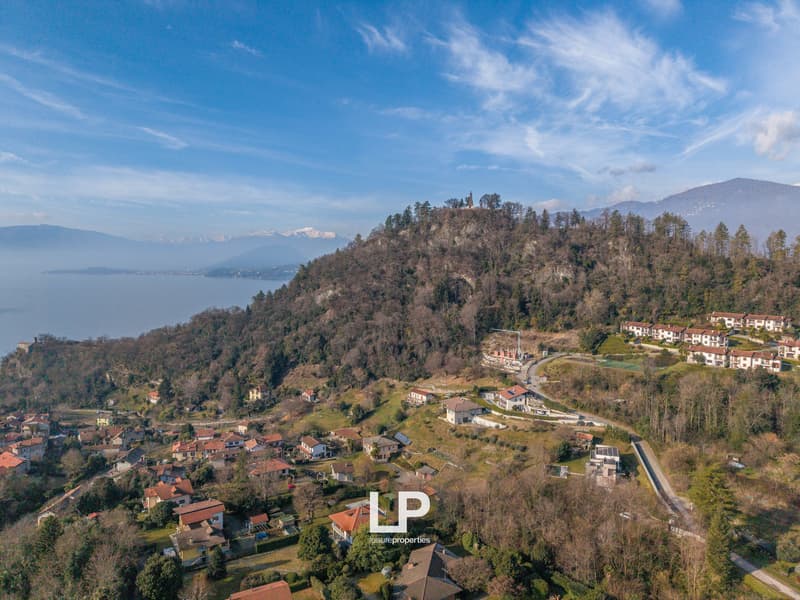 Multiple residential houses in a mountain village, surrounded by hills and a lake, under a blue sky