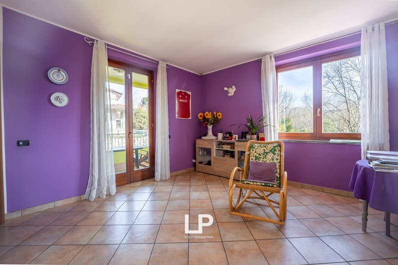 room with purple walls, a tile floor, a large window, a glass door leading to a balcony, a wooden chair, a cabinet, a table with books