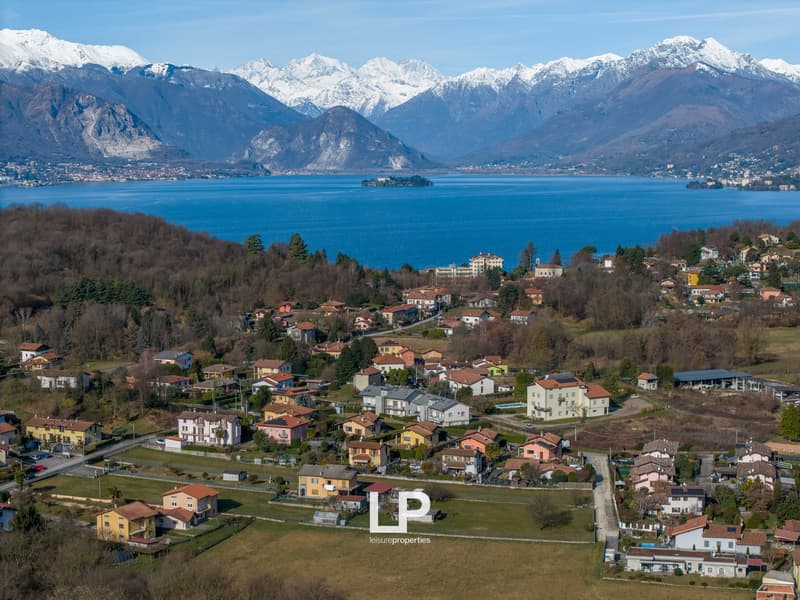 Overview of residential area with houses, greenery, mountains, and a large lake in the distance
