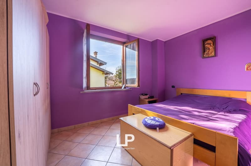 Bedroom with purple walls, wooden bed, bedside table, bedside lamp, wooden storage bench, window, tiled floor, wooden wardrobe
