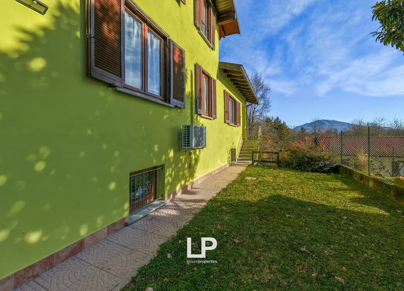 lime green building with wooden shutters, paved pathway, small garden, outdoor air conditioning unit