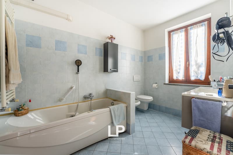 white bathtub, toilet, washbasin, tiled wall and floor, window with curtains, shelves and toiletries