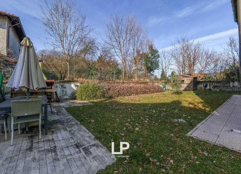 a garden with a small patio area, outdoor table and chairs, an umbrella, and some greenery