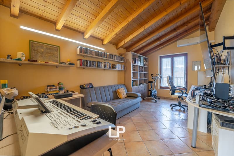 Living room with exposed wooden beams, light colored tiles, desk with piano, sofa, books on shelves, window with view, office chair, treadmill, desk with computer setup