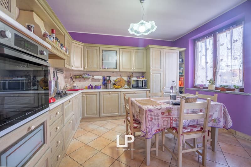 Cabinets and drawers in light wood, kitchen appliances including oven, dishwasher, microwave, tile flooring, breakfast table with chairs, window with curtain