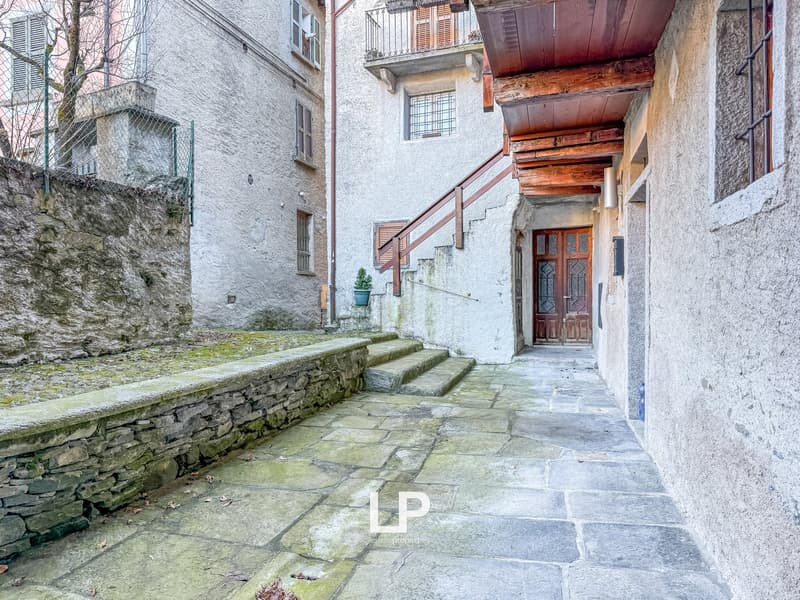 stone wall, cobblestone path, stairs, wooden balcony, potted plant, doorway