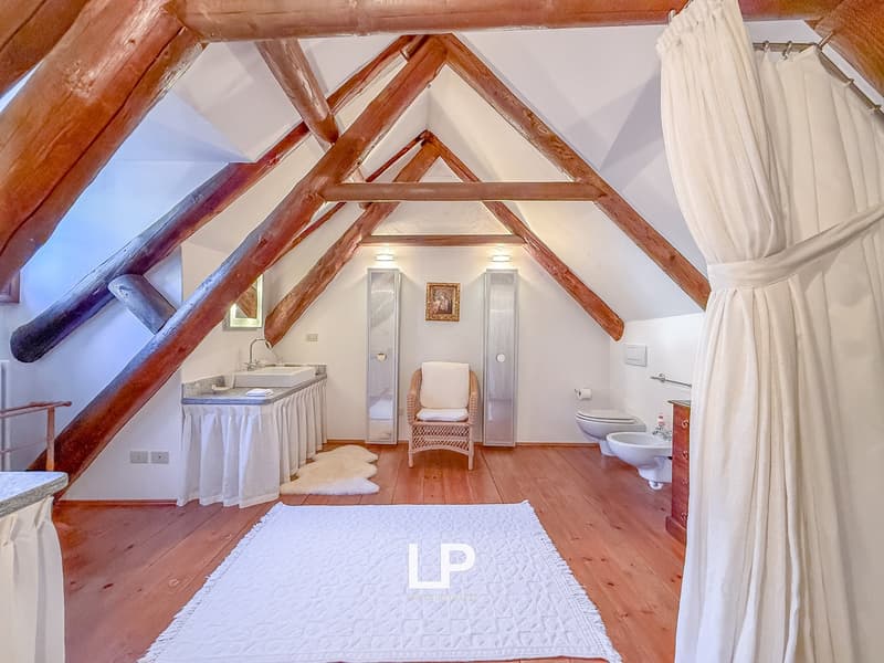 Atrium bathroom with wooden beams, white walls, wooden floor, white ceiling, wooden furniture, white towels, white sink, modern fixtures