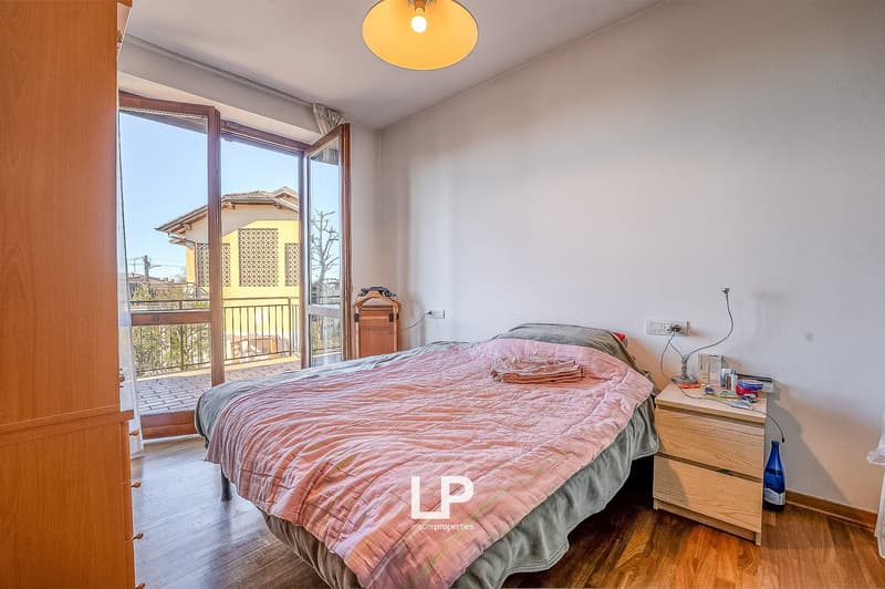 large bed, white walls, wooden floor, nightstand, bedside lamp, bedside lamp plug, sliding glass door leading to balcony