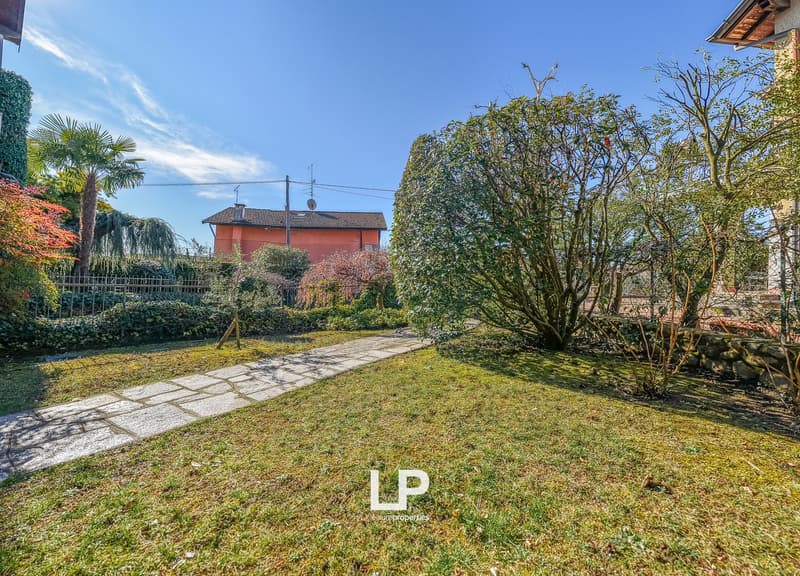 Garden with a lawn, trees, plants, a brick pathway, and a building in the background
