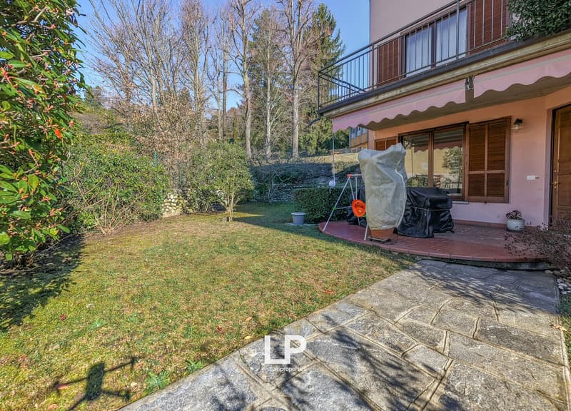 Lawn, paved walkway, covered terrace with railings, greenery, house with balcony