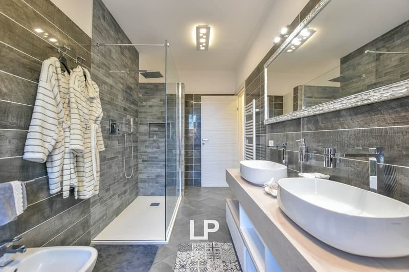 2 sinks, shower with glass enclosure, towel racks, large mirror, ceramic floor, illuminated tiles, and a towel