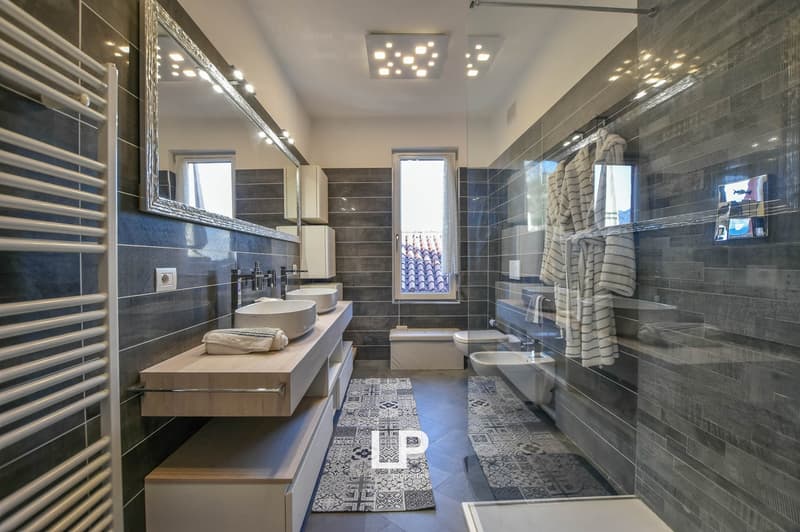 Bathroom with gray tiles, white sinks, toilet, bathtub, and shower; also features a large mirror and towel rack.
