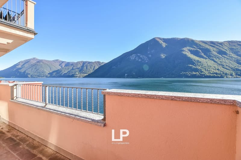 Outdoor balcony with metal railing, pink wall, overlooking water and mountains.