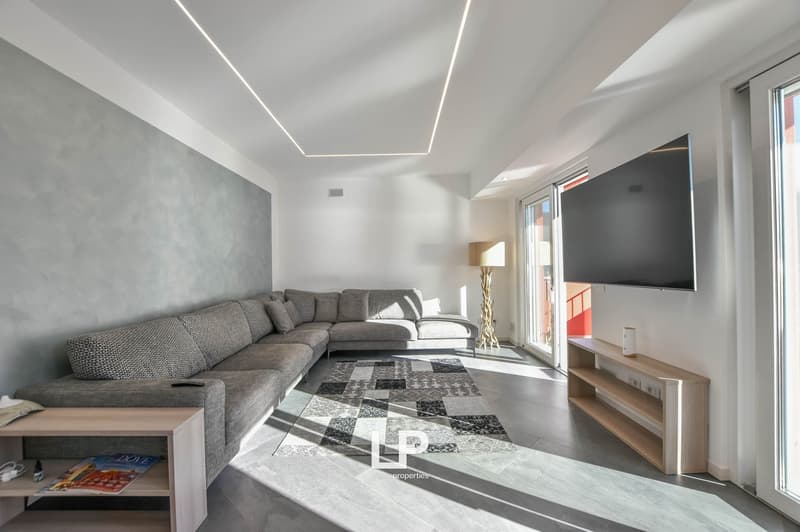 Gray sofa, gray and black rug, wooden coffee table, TV, wall lamp, floor outlets, large windows