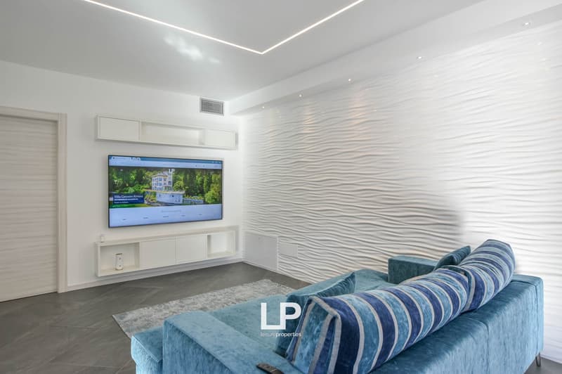 modern living room with grey floor, white wave textured wall, large TV, built-in shelves, blue sofa with cushions