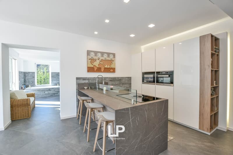 Modern kitchen with granite countertops, central island with built-in stove and seating, open layout to living area, white cabinetry, recessed lighting