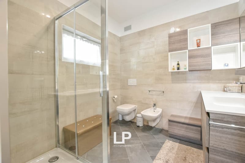 Modern shower enclosure, white tiled wall, glass walk-in shower, sink, floor with benches and shelves