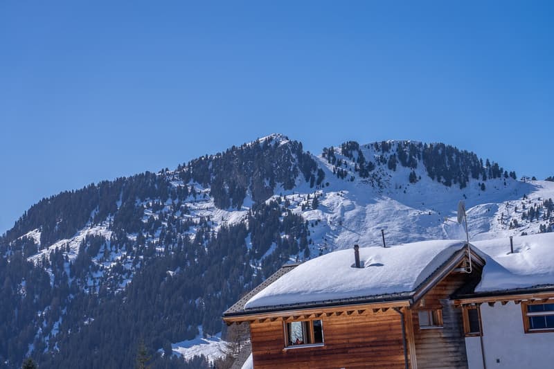wooden chalet, snow on the roof, snowy mountain in the background