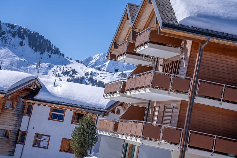 wooden exterior, multiple balconies, snow on the roof, mountain in the background