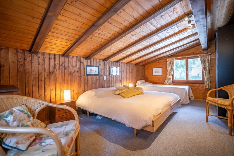 bedroom with wooden walls, two beds, nightstands, lamps, chair, carpet, window with curtains