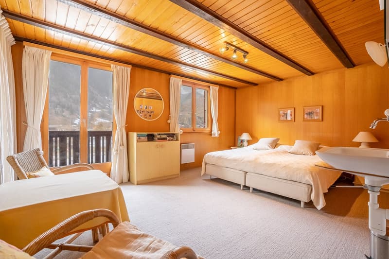 bedroom with bed, desk, chairs, lamps, mirror, wooden walls, balcony, window, radiator