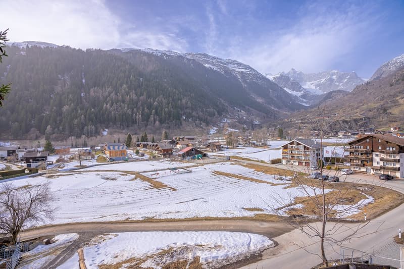 Mountain village with several chalets, snow-covered fields, and a scenic view of the mountains