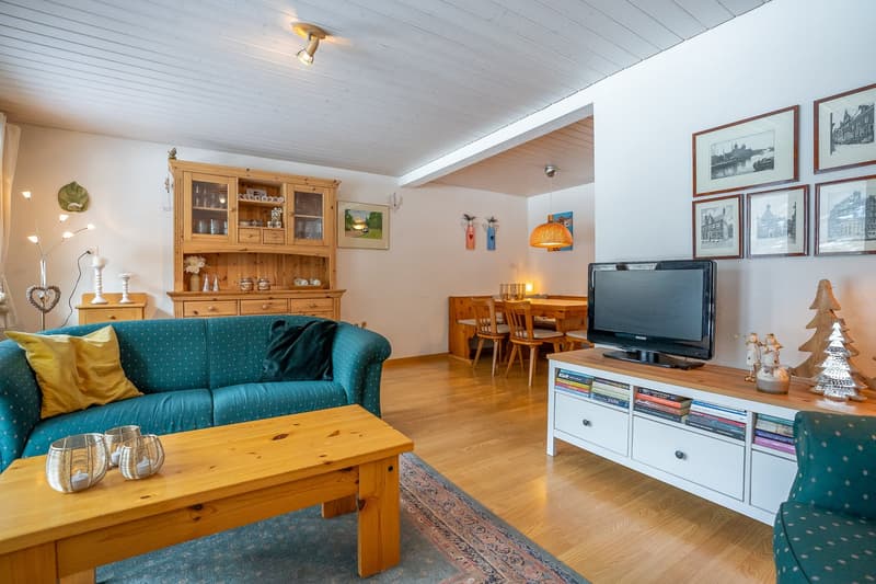 living room with wooden floor, blue sofa, wooden coffee table, TV, wooden cabinet, dining table, wooden chairs, wooden TV stand, picture frames, Christmas tree