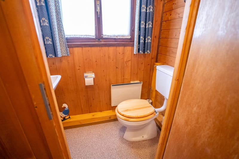 wooden walls, white toilet, white sink, window with blue curtains, wooden floor