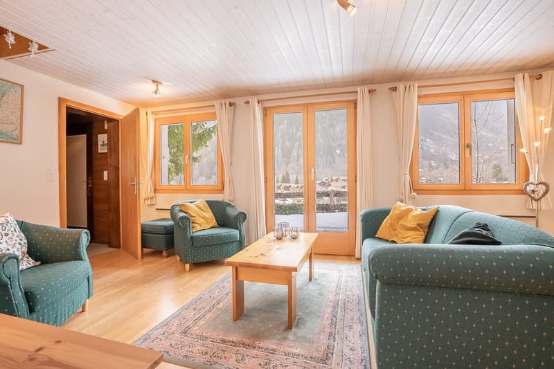 living room with wooden floor, two green sofas, coffee table, rug, large windows, view of mountains